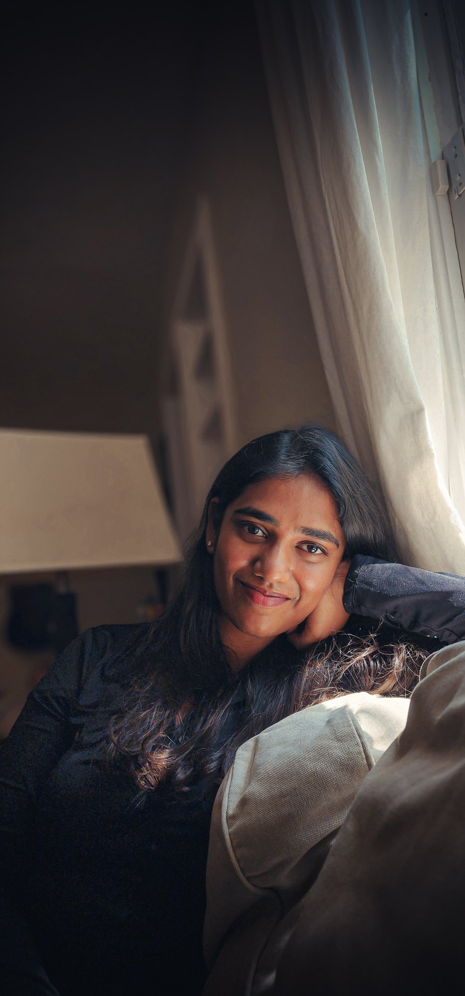 Soft window light falling across a young woman by the curtains