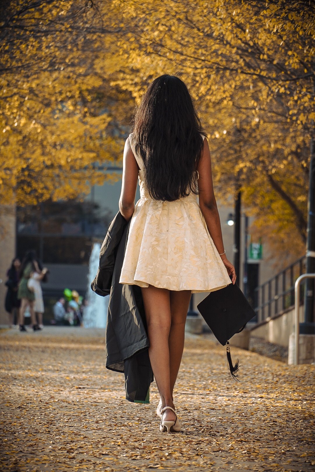 A graduate walking through golden autumn leaves